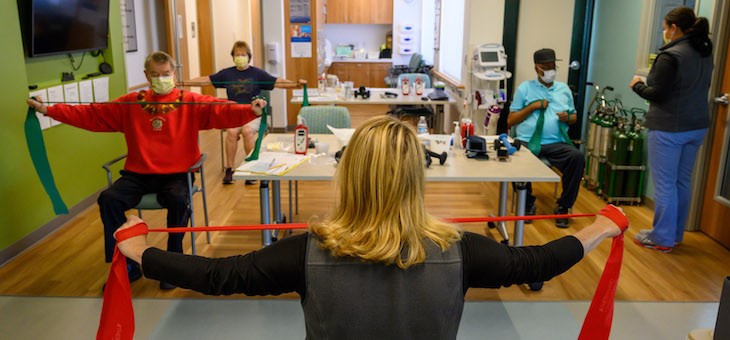 People exercising in chairs with colorful bands during a pulmonary rehabilitation class